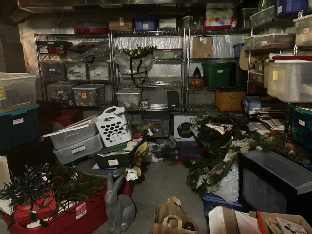 Before — basement floor covered with garland, wreaths and string lights beside full bins, basement in Independence, KY
