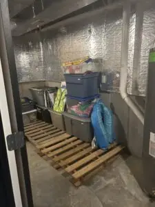After — lidded bins stacked on wooden pallets with games on top and pool floats hung at the side, basement storage room in Union, KY