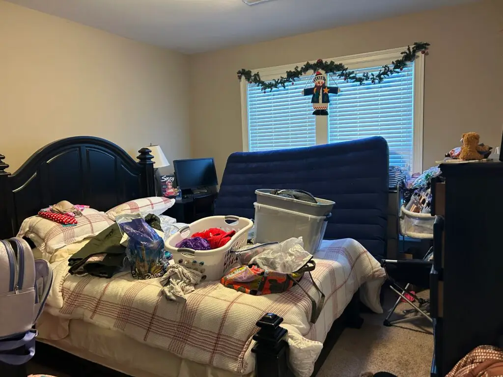 Before — an air mattress standing on end across the bed with a laundry basket, a tub and bags in front of it, guest bedroom in Union, KY