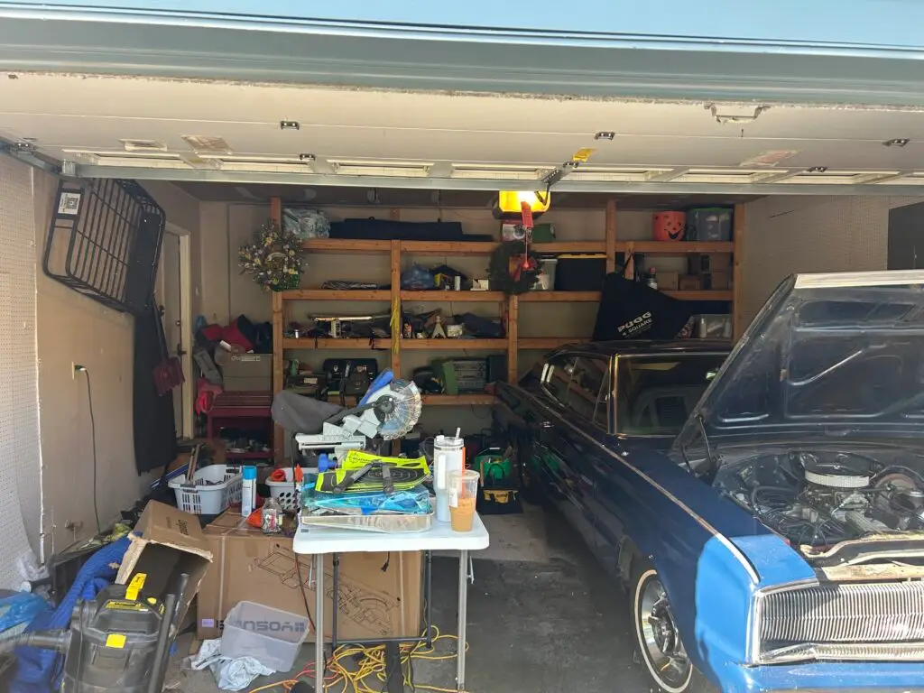 Before — a folding table covered in tools beside a miter saw, with boxes and a shop vac on the floor next to a classic blue car, garage in Crescent Springs, KY