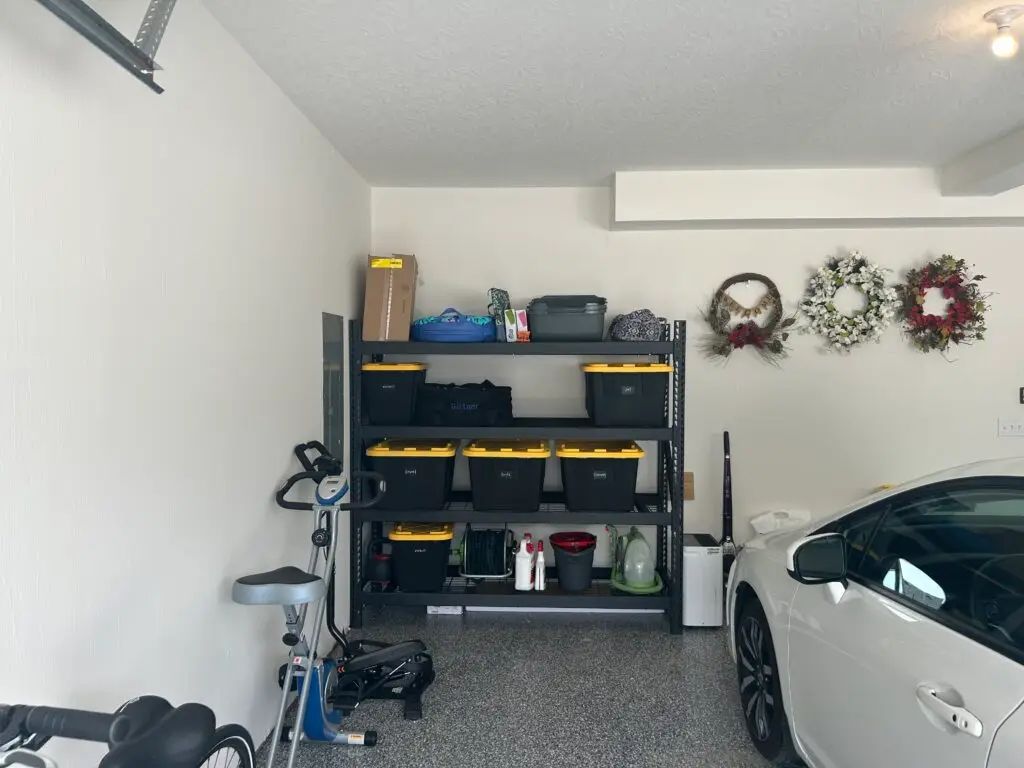 After — one black shelving unit of labeled yellow-lidded bins, wreaths hung on the wall and a car parked on a clear floor, garage in Union, KY