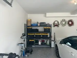 After — one black shelving unit of labeled yellow-lidded bins, wreaths hung on the wall and a car parked on a clear floor, garage in Union, KY