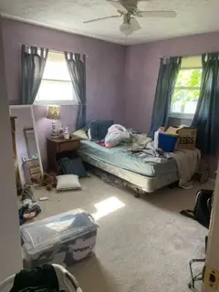 Before — a bare mattress with papers and a laptop on it and boxes across the carpet, guest bedroom in Cincinnati, OH