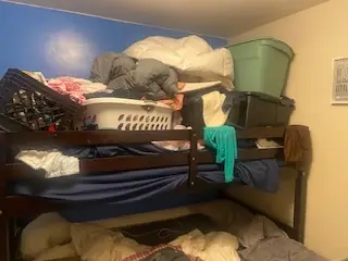 Before — the top bunk stacked with bedding, a laundry basket, bins and a crate, kids bedroom in Cincinnati, OH