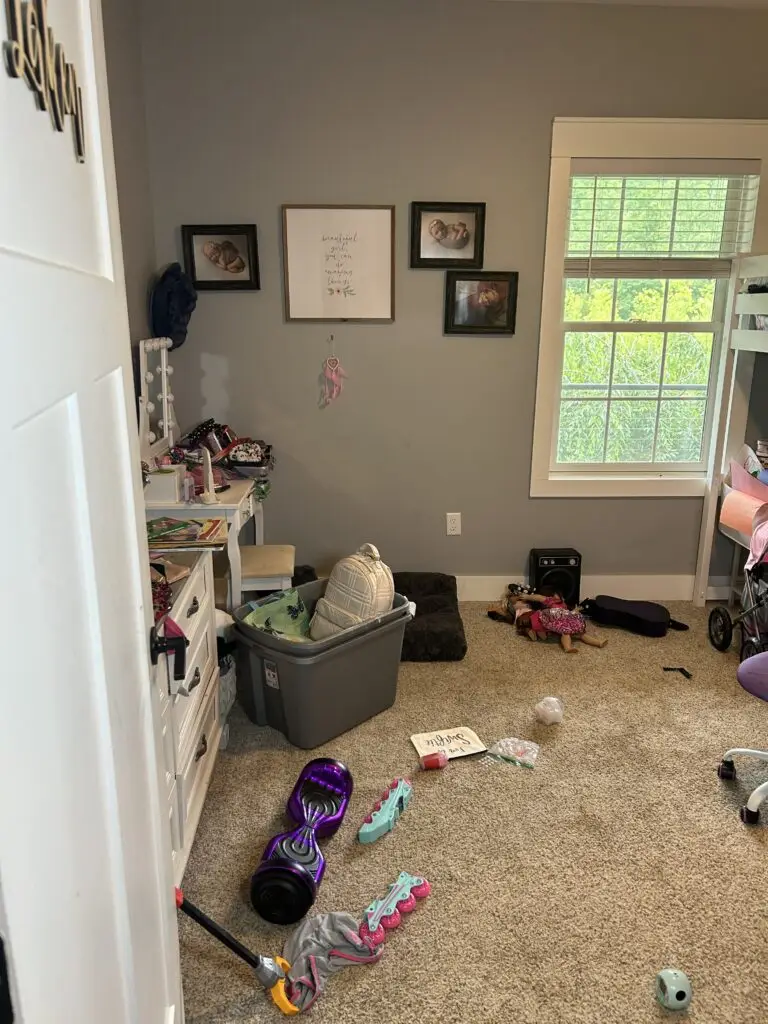 Before — toys, a bin and clothing across the carpet seen from the doorway, girl's bedroom in Covington, KY