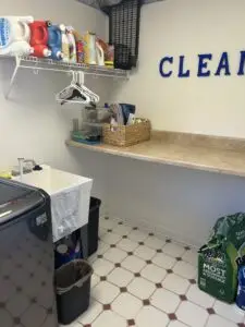 After — a clear folding counter with a wicker basket, detergents lined on the wire shelf and hangers hung beneath it, laundry room in Alexandria, KY