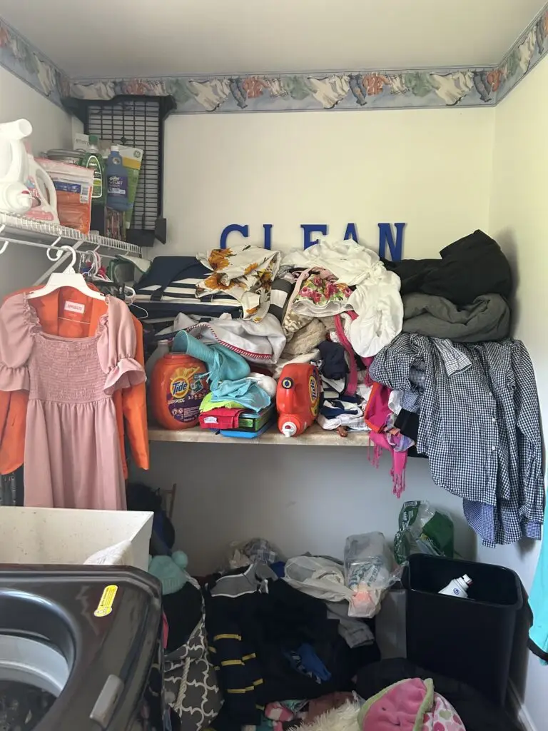 Before — clean laundry heaped along the folding counter with detergent tubs in the middle and bags on the floor, laundry room in Alexandria, KY