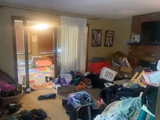 Before — clothes and bags covering the floor from the doorway to the sliding door, living room in Cincinnati, OH