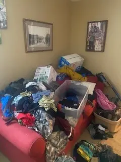 Before — a red sofa buried under clothes, boxes and bins, living room in Cincinnati, OH