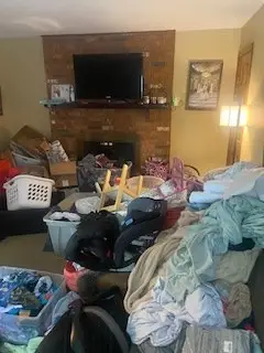 Before — bedding and clothes heaped on the sofa and floor in front of a brick fireplace, living room in Cincinnati, OH