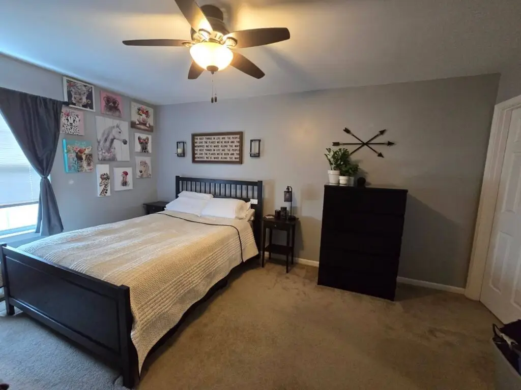After — a made bed with a cream coverlet, a clear carpet and plants on the dresser under the gallery wall, master bedroom in Park Hills, KY