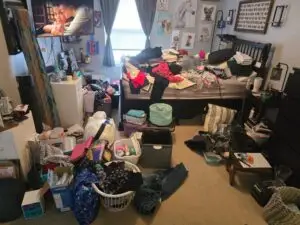 Before — clothes heaped on the bed with laundry baskets, bins and boxes covering the carpet, master bedroom in Park Hills, KY
