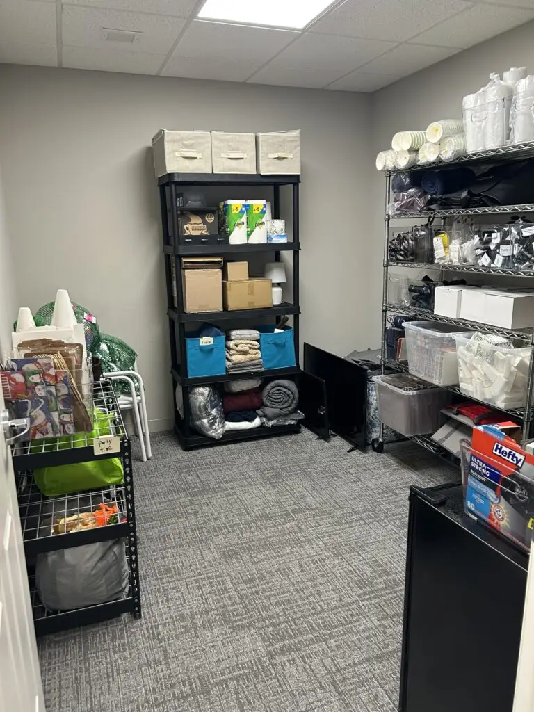 After — a clear carpet between a labeled black shelving unit, a stocked chrome wire rack and a party-supplies cart, senior living storage room in Union, KY