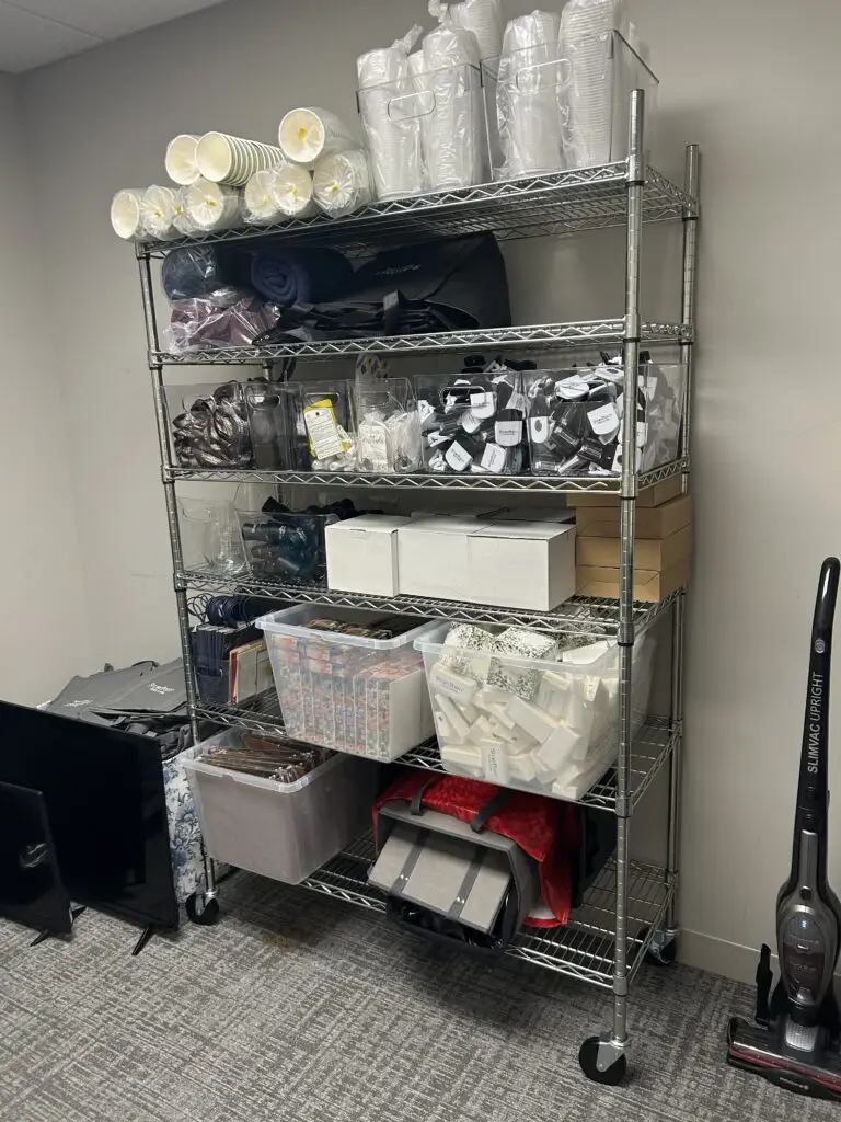 After — chrome wire rack with cups and lids in clear bins, packaged supplies sorted by type and folded blankets bagged, senior living storage room in Union, KY